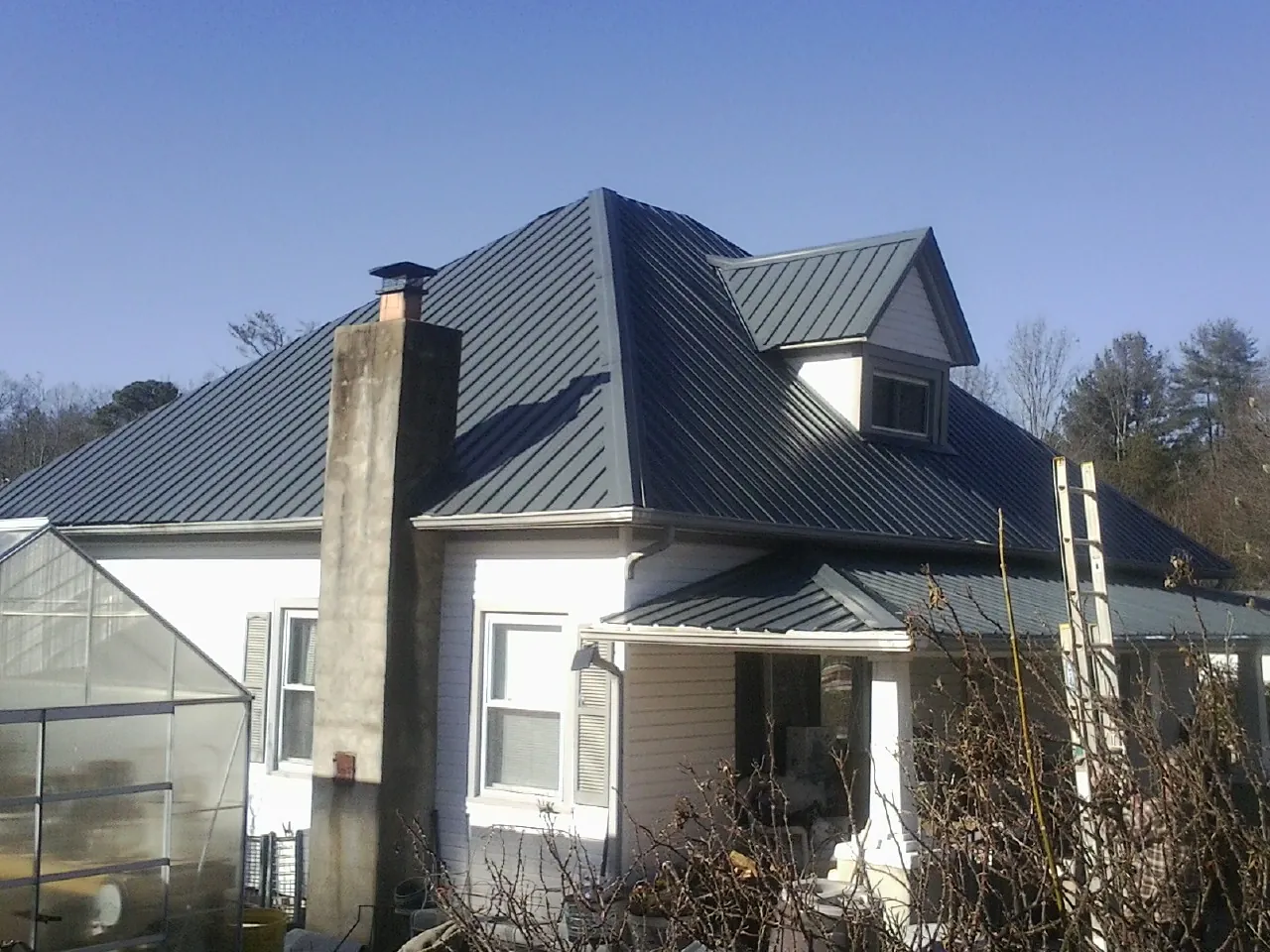 Dark blue standing seam metal roof on a white farmhouse with dormer — Slate & Tile Roof Repair by Roofing Brothers in Dow City