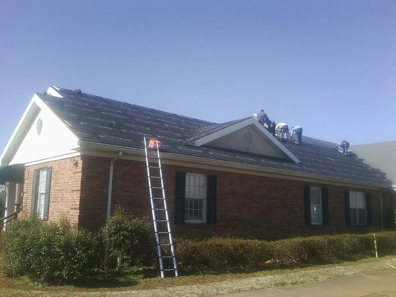 Crew tearing shingles off a brick ranch roof with a ladder set — Emergency Roof Repair work by our crew in Dow City