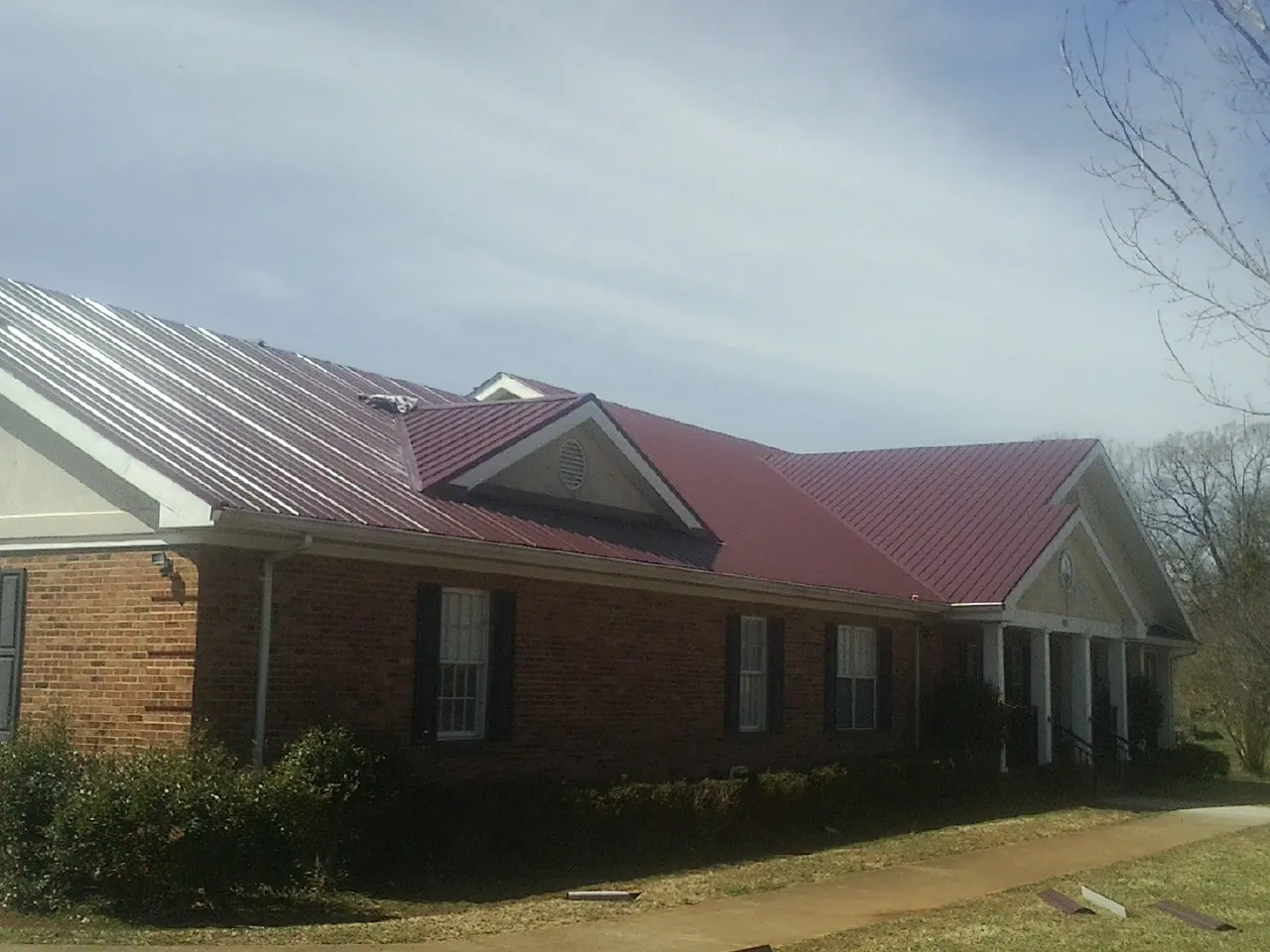 Red metal roof with gabled entries on a long brick building, from a Hail Damage Roof Repair job in Dow City