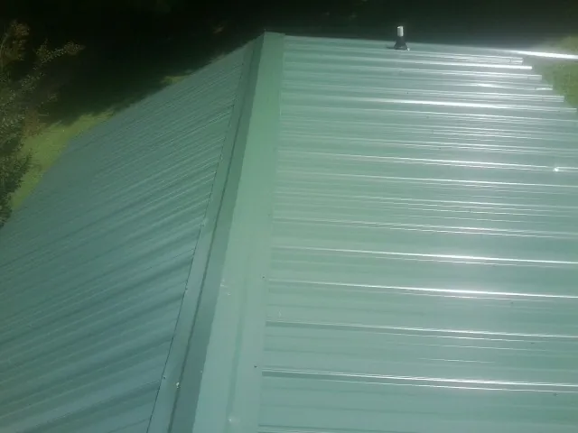 New green metal panels meeting at the ridge of a roof — Flat Roof Repair work by our crew in Dow City