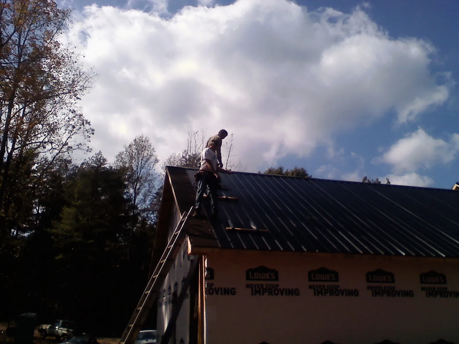 Roofer fastening dark metal panels high against a cloudy sky, from a Roof Inspection job in Dow City