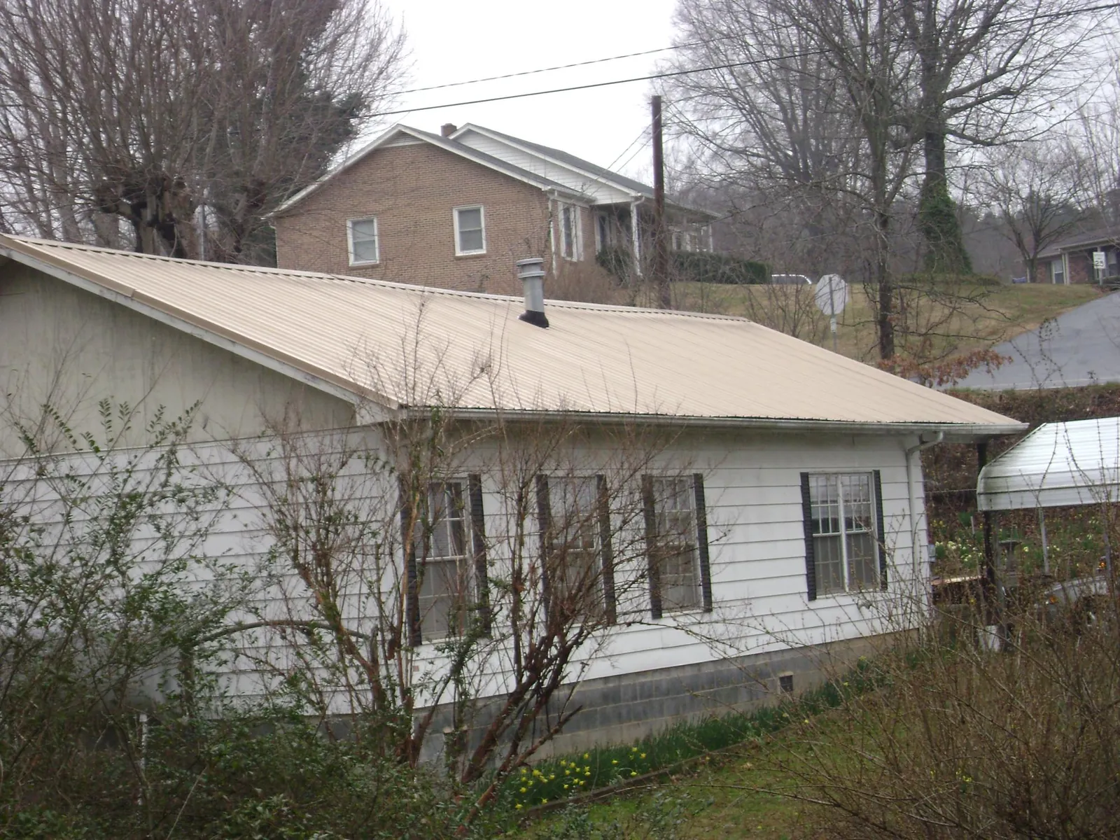 Tan metal roof on a white sided house set into a hillside — Commercial Roofing by Roofing Brothers in Dow City