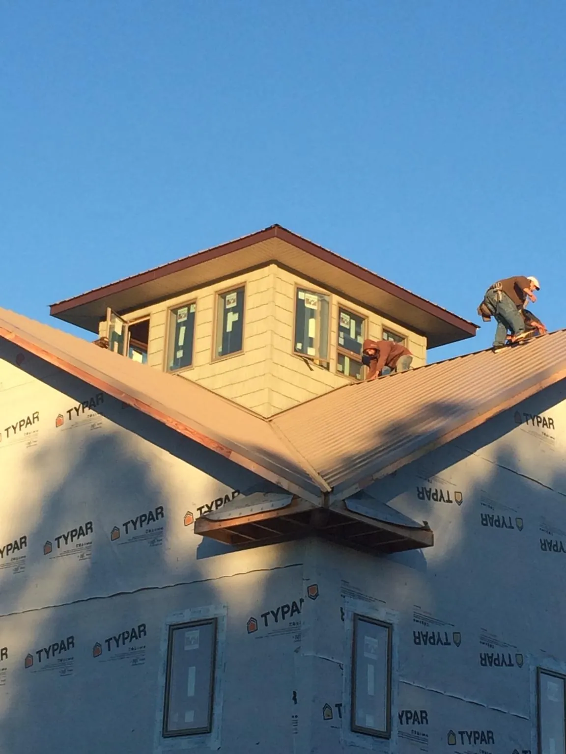 Roofers working around a rooftop cupola on a new metal roof at sunset in Dow City